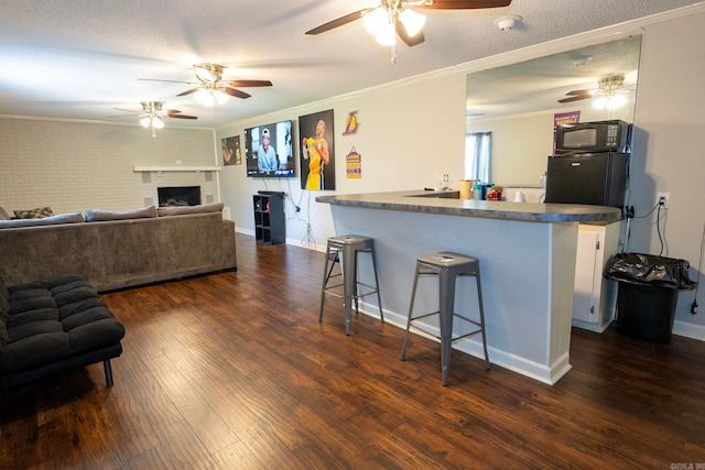 kitchen featuring a kitchen bar, a textured ceiling, a brick fireplace, brick wall, and dark hardwood / wood-style flooring