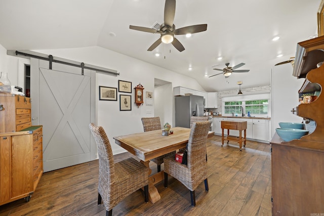 dining room with dark hardwood / wood-style flooring, a barn door, ceiling fan, and vaulted ceiling