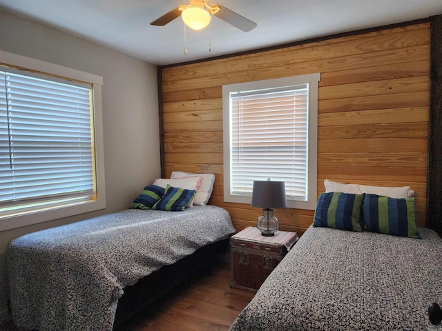 bedroom featuring wood-type flooring, wood walls, multiple windows, and ceiling fan