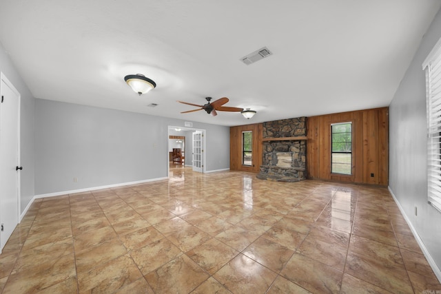 unfurnished living room featuring a stone fireplace, ceiling fan, and light tile patterned floors