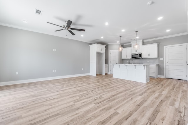 kitchen featuring white cabinetry, hanging light fixtures, light wood-type flooring, an island with sink, and ceiling fan