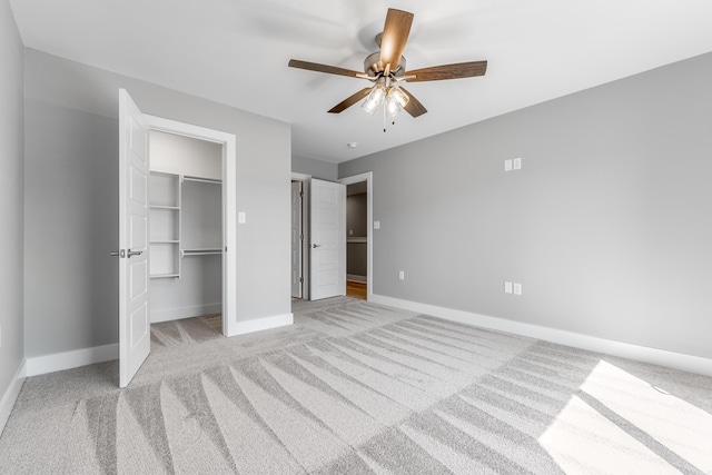 unfurnished bedroom with ceiling fan, a spacious closet, a closet, and light carpet