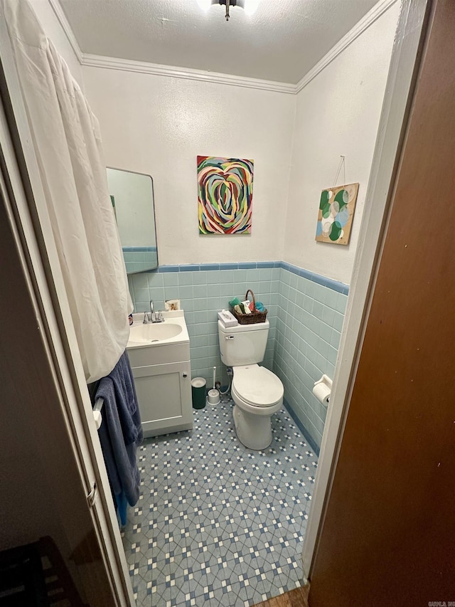 bathroom with toilet, tile walls, vanity, and ornamental molding