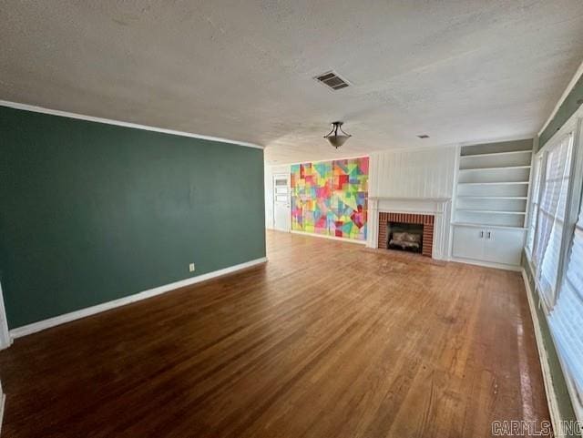 unfurnished living room with built in shelves, hardwood / wood-style floors, a fireplace, and a textured ceiling