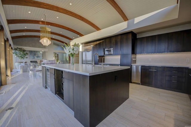 kitchen with hanging light fixtures, a notable chandelier, an island with sink, vaulted ceiling, and brick ceiling