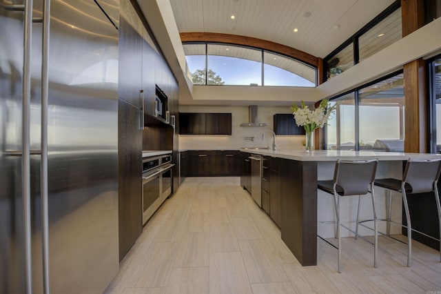 kitchen featuring sink, wall chimney exhaust hood, stainless steel appliances, vaulted ceiling, and brick ceiling