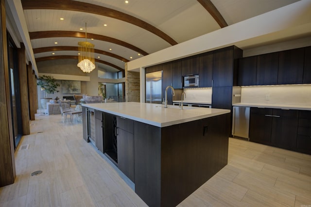 kitchen featuring an inviting chandelier, decorative light fixtures, lofted ceiling, brick ceiling, and a kitchen island with sink