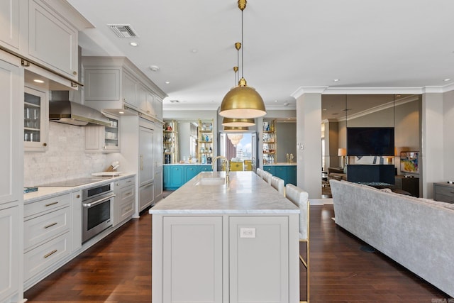 kitchen with backsplash, oven, crown molding, a kitchen island with sink, and dark hardwood / wood-style flooring