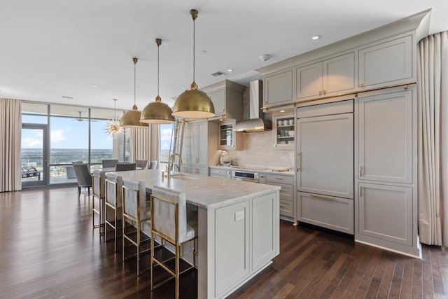 kitchen featuring pendant lighting, wall chimney exhaust hood, sink, dark hardwood / wood-style floors, and a kitchen island with sink