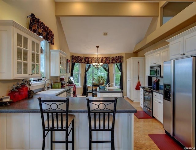 kitchen featuring kitchen peninsula, appliances with stainless steel finishes, decorative light fixtures, white cabinetry, and a kitchen bar