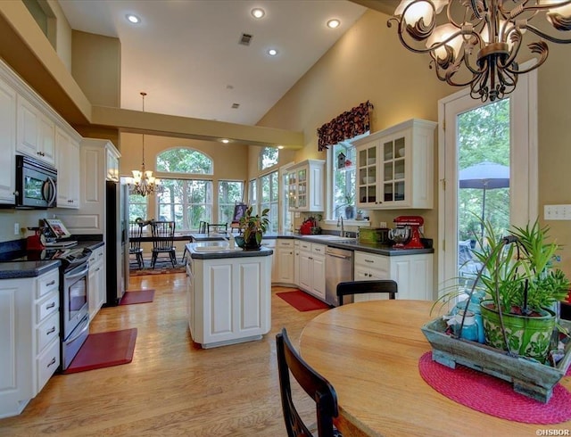 kitchen with appliances with stainless steel finishes, a chandelier, white cabinets, decorative light fixtures, and a high ceiling