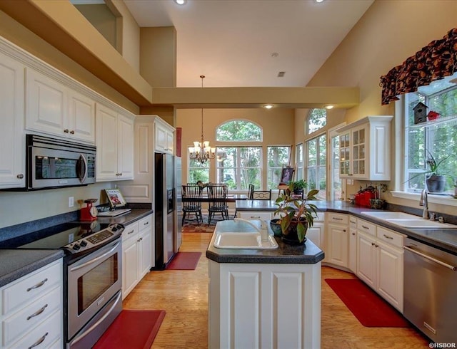 kitchen featuring a towering ceiling, appliances with stainless steel finishes, white cabinetry, sink, and a kitchen island