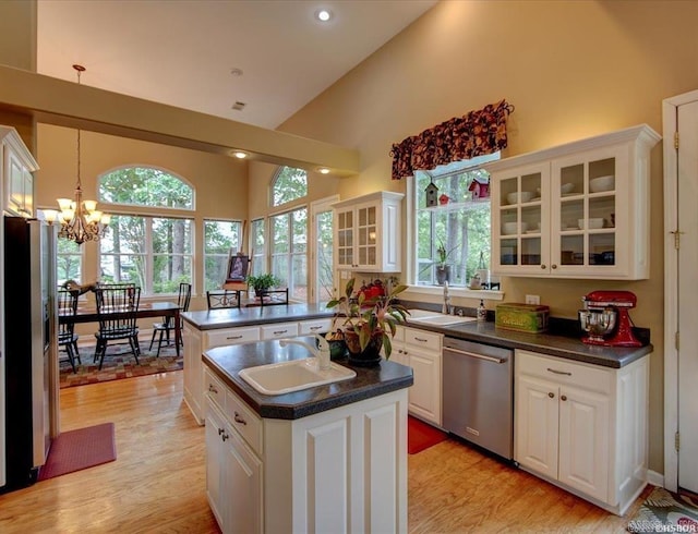 kitchen with light hardwood / wood-style floors, white cabinetry, hanging light fixtures, stainless steel appliances, and a center island with sink