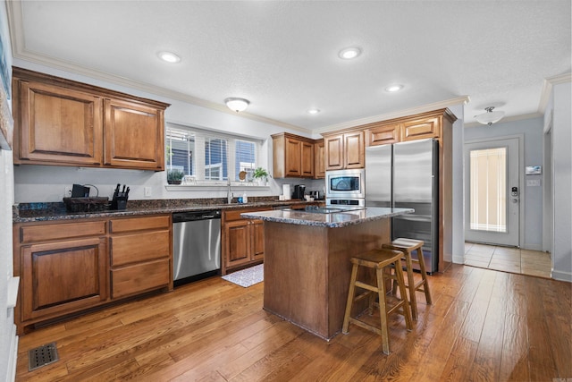 kitchen with crown molding, stainless steel appliances, visible vents, light wood-style floors, and brown cabinetry