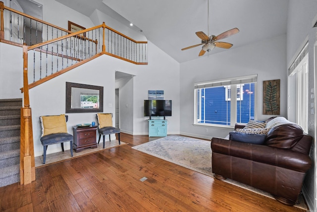 living area with baseboards, a ceiling fan, wood-type flooring, stairway, and a high ceiling