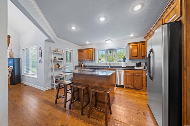 kitchen with a breakfast bar area, light wood-style flooring, a sink, appliances with stainless steel finishes, and brown cabinetry