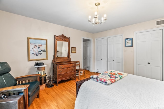 bedroom featuring a chandelier, light hardwood / wood-style floors, and two closets