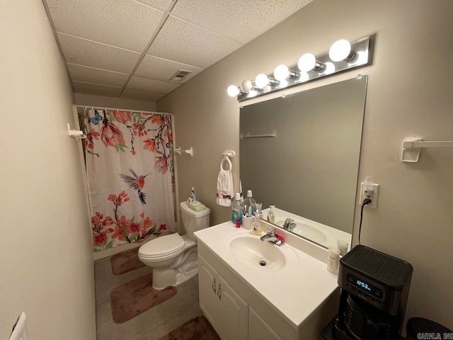 bathroom with tile patterned flooring, a drop ceiling, toilet, and vanity