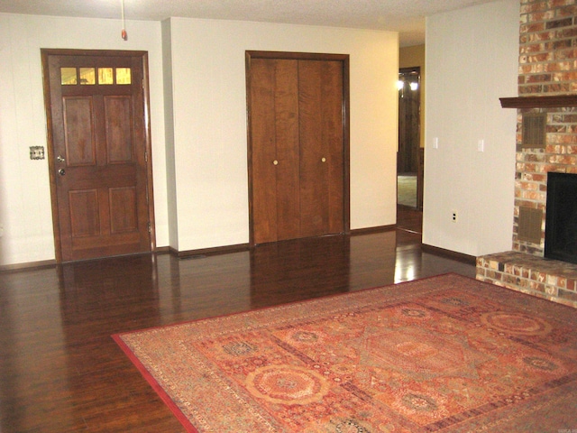901 Hastey Ave, Mena, AR 71953 - unfurnished living room with a brick fireplace, baseboards, and dark wood-style flooring
