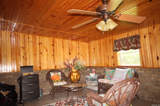 living area with wooden ceiling, tile patterned flooring, ceiling fan, wood walls, and brick wall