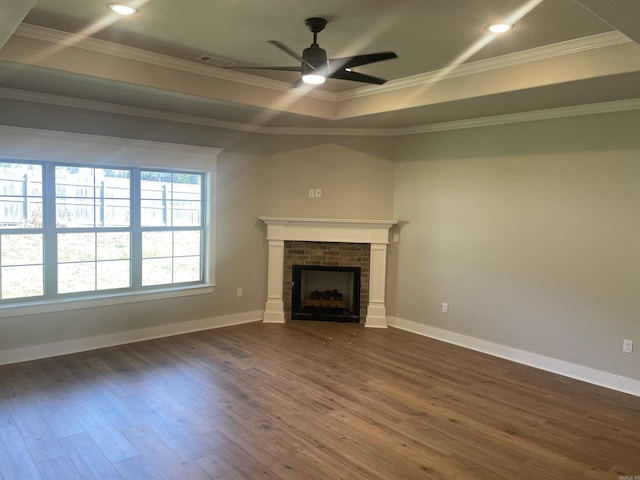 unfurnished living room featuring a brick fireplace, ornamental molding, dark hardwood / wood-style floors, a raised ceiling, and ceiling fan