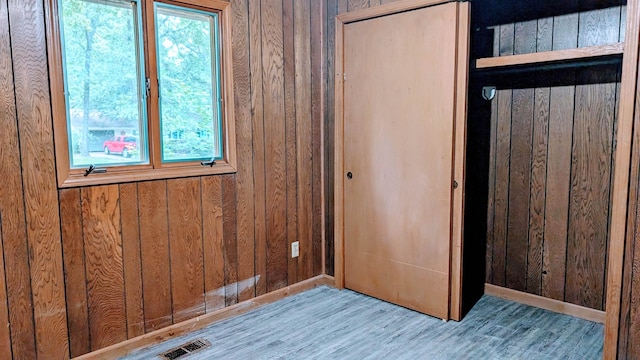 unfurnished bedroom with multiple windows, wooden walls, and wood-type flooring