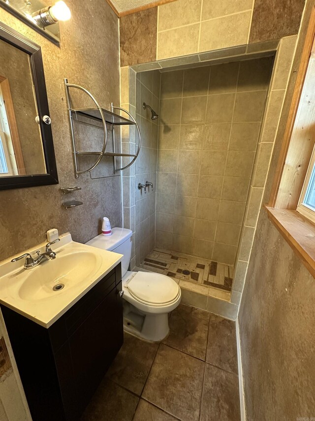 bathroom featuring toilet, tile patterned flooring, tiled shower, and vanity