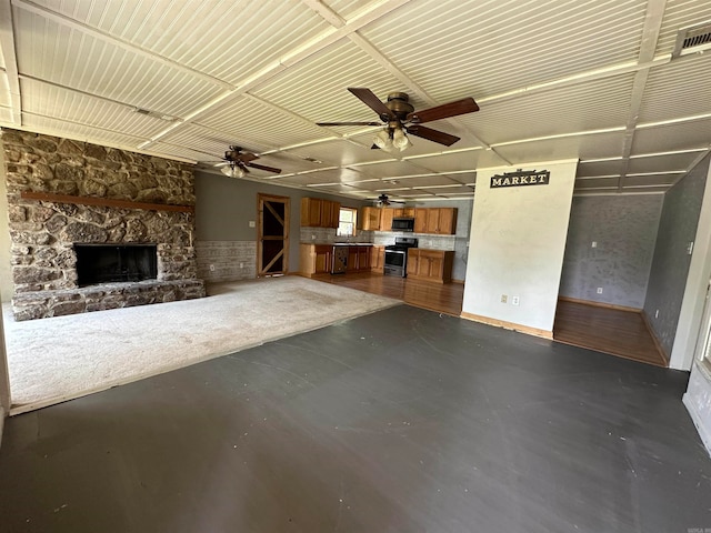 unfurnished living room featuring concrete flooring, a stone fireplace, and ceiling fan