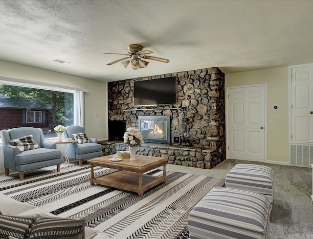 carpeted living room with ceiling fan, a textured ceiling, and a stone fireplace