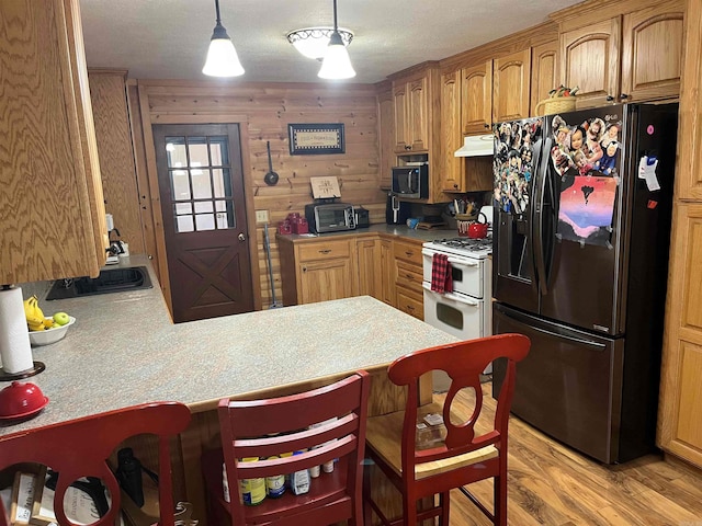 kitchen featuring a kitchen bar, gas range gas stove, kitchen peninsula, wood walls, and black refrigerator with ice dispenser