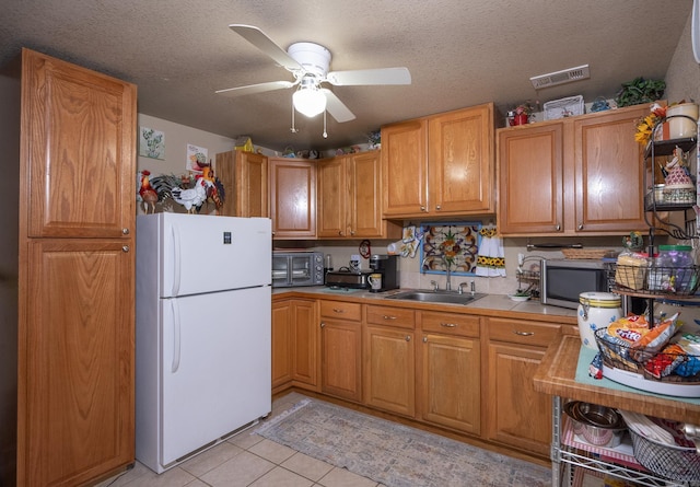 kitchen featuring a textured ceiling, white fridge, sink, ceiling fan, and light tile patterned floors