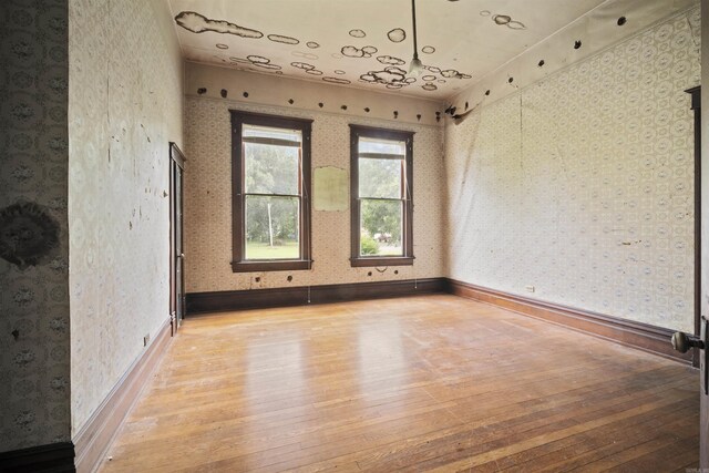 empty room featuring light wood-type flooring, baseboards, and wallpapered walls