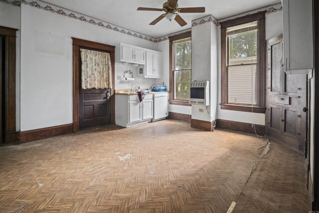 kitchen featuring baseboards, light countertops, heating unit, white cabinetry, and a ceiling fan