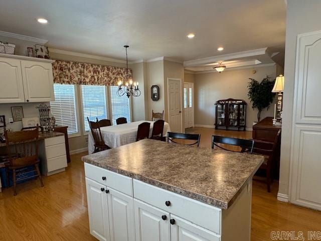 kitchen featuring pendant lighting, light hardwood / wood-style floors, a kitchen island, crown molding, and white cabinets