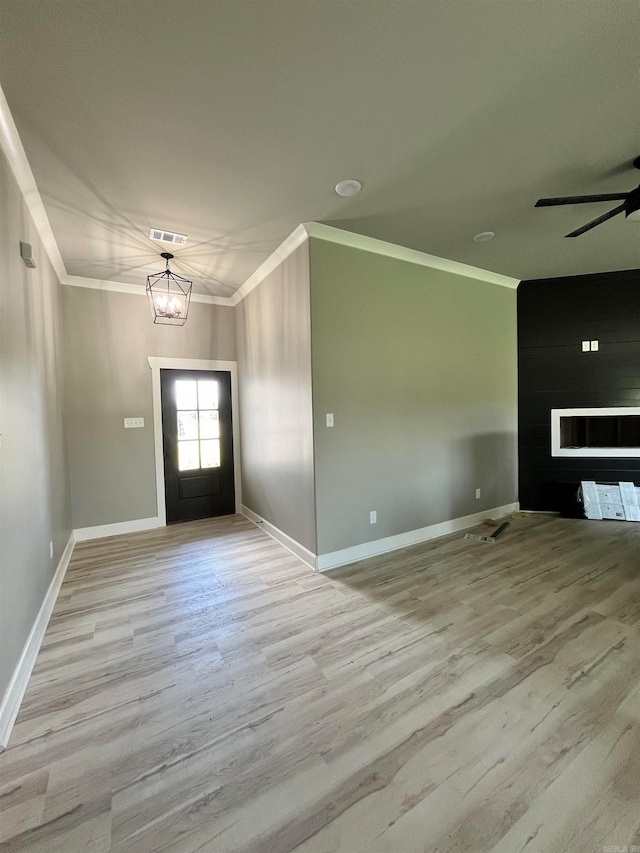 foyer entrance featuring ceiling fan with notable chandelier, light hardwood / wood-style flooring, ornamental molding, and a fireplace