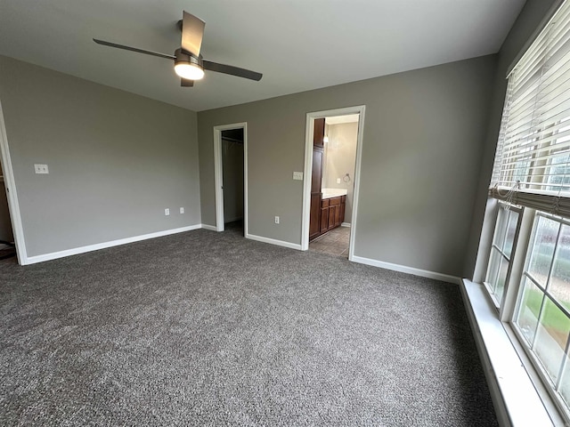 unfurnished bedroom featuring ceiling fan, ensuite bathroom, and dark carpet