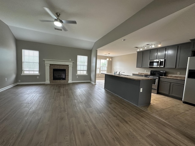 kitchen featuring a center island with sink, appliances with stainless steel finishes, gray cabinetry, ceiling fan with notable chandelier, and light hardwood / wood-style flooring