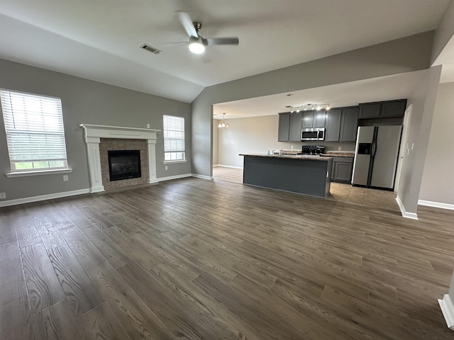 unfurnished living room with vaulted ceiling, dark wood-type flooring, a fireplace, and ceiling fan with notable chandelier