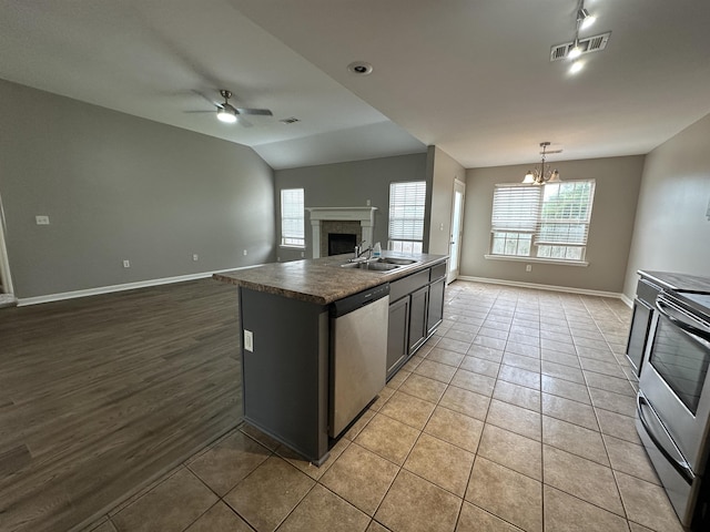 kitchen featuring sink, a kitchen island with sink, appliances with stainless steel finishes, light tile patterned floors, and ceiling fan with notable chandelier