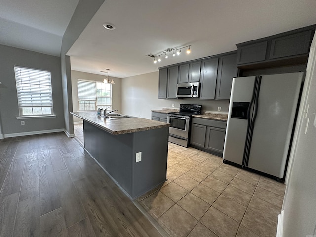 kitchen featuring pendant lighting, appliances with stainless steel finishes, an island with sink, gray cabinets, and a chandelier