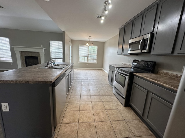 kitchen featuring a notable chandelier, a center island with sink, sink, appliances with stainless steel finishes, and light tile patterned floors