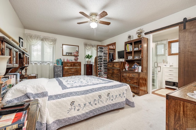 bedroom featuring ceiling fan, a barn door, carpet floors, ensuite bathroom, and a textured ceiling