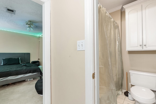 bathroom with toilet, ornamental molding, a textured ceiling, and tile patterned flooring