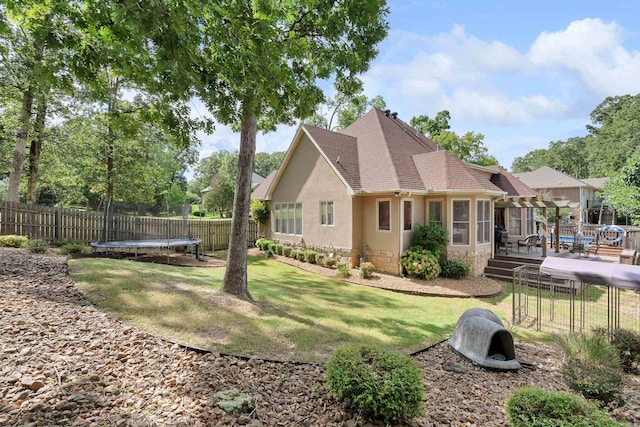 back of house featuring a wooden deck, a yard, and a trampoline