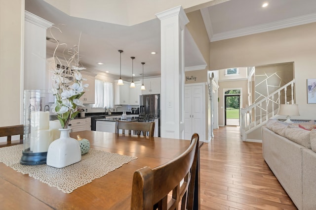 dining area with decorative columns, crown molding, and light wood-type flooring