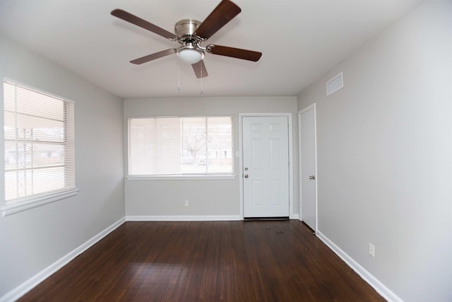 empty room featuring ceiling fan, a wealth of natural light, and dark hardwood / wood-style flooring