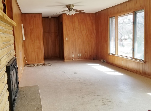 unfurnished living room with a stone fireplace, ceiling fan, and wooden walls