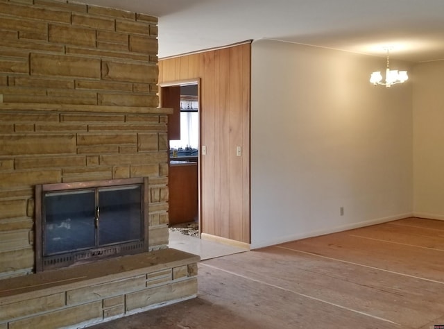 unfurnished living room featuring hardwood / wood-style flooring, a fireplace, wood walls, and a notable chandelier