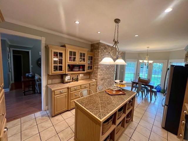 kitchen with pendant lighting, a center island, stainless steel fridge, light tile patterned floors, and crown molding