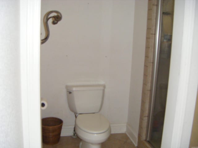 bathroom featuring toilet, tile patterned flooring, and a shower with shower door